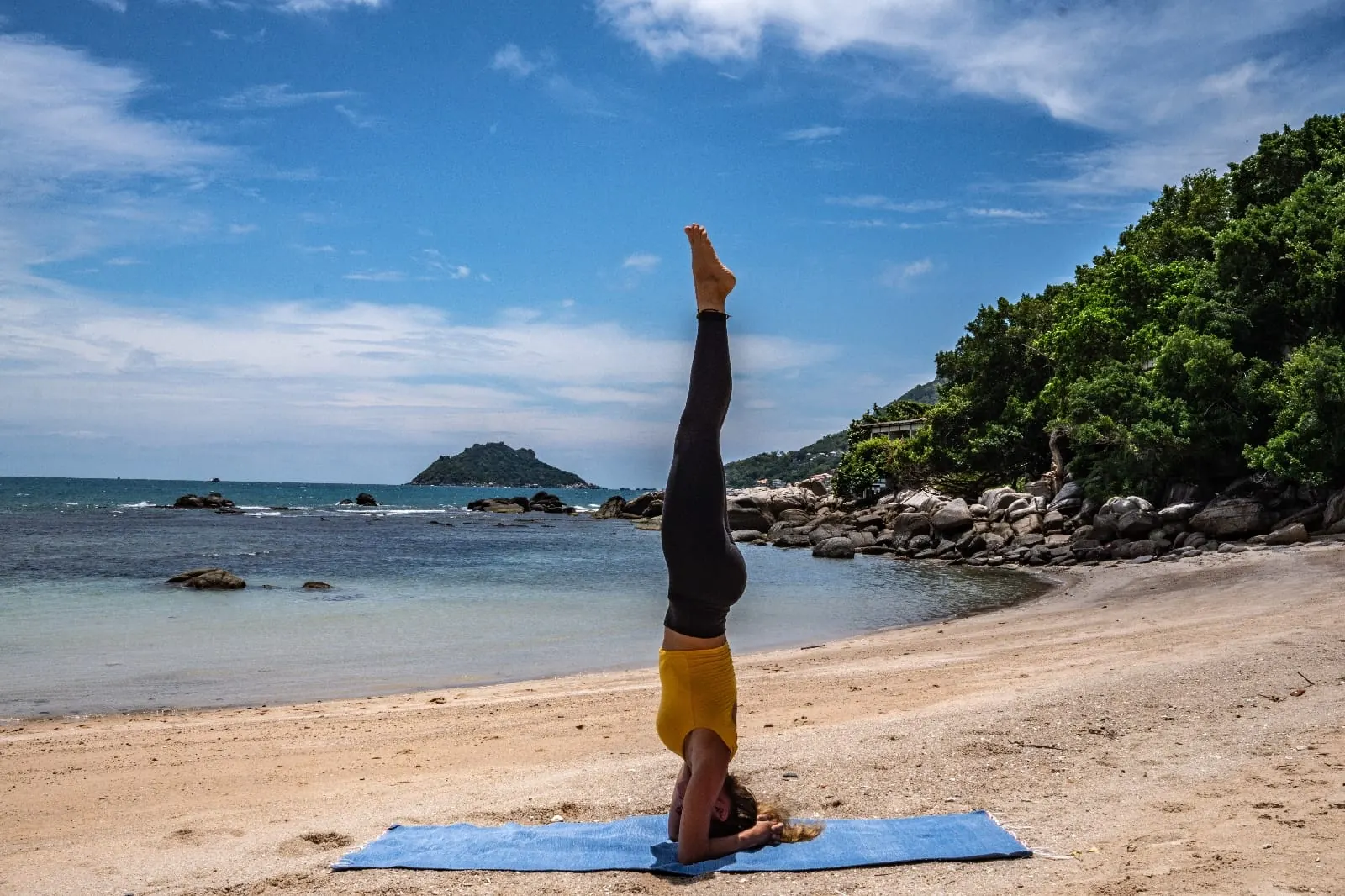 A headstand on a yoga mat on the beach with the sea behind