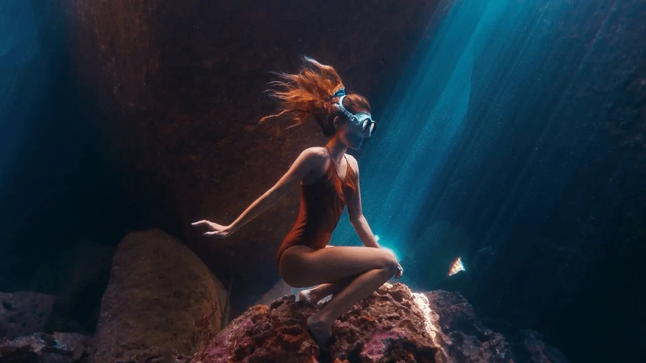 A freediver inside an underwater cave lit by sunbeams