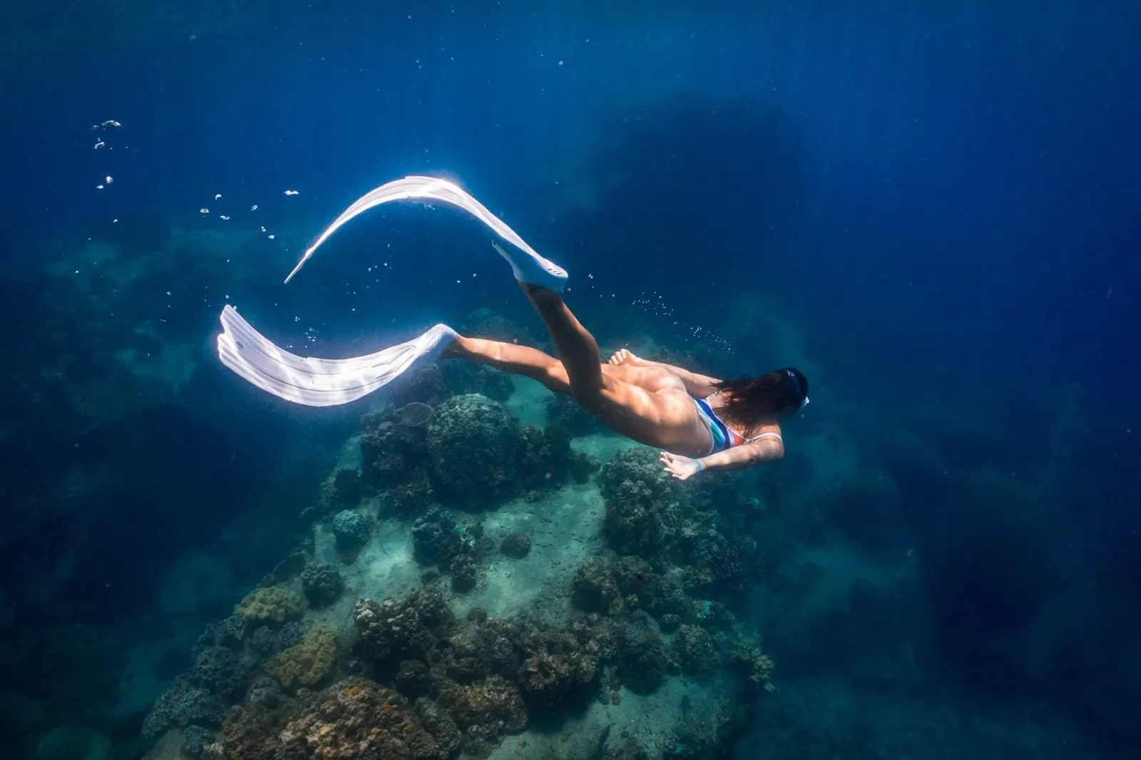 A freediver with a white monofin gliding above a coral pinnacle