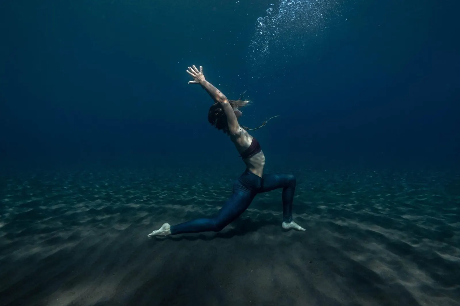 A freediver holding a yoga pose on the sandy sea floor